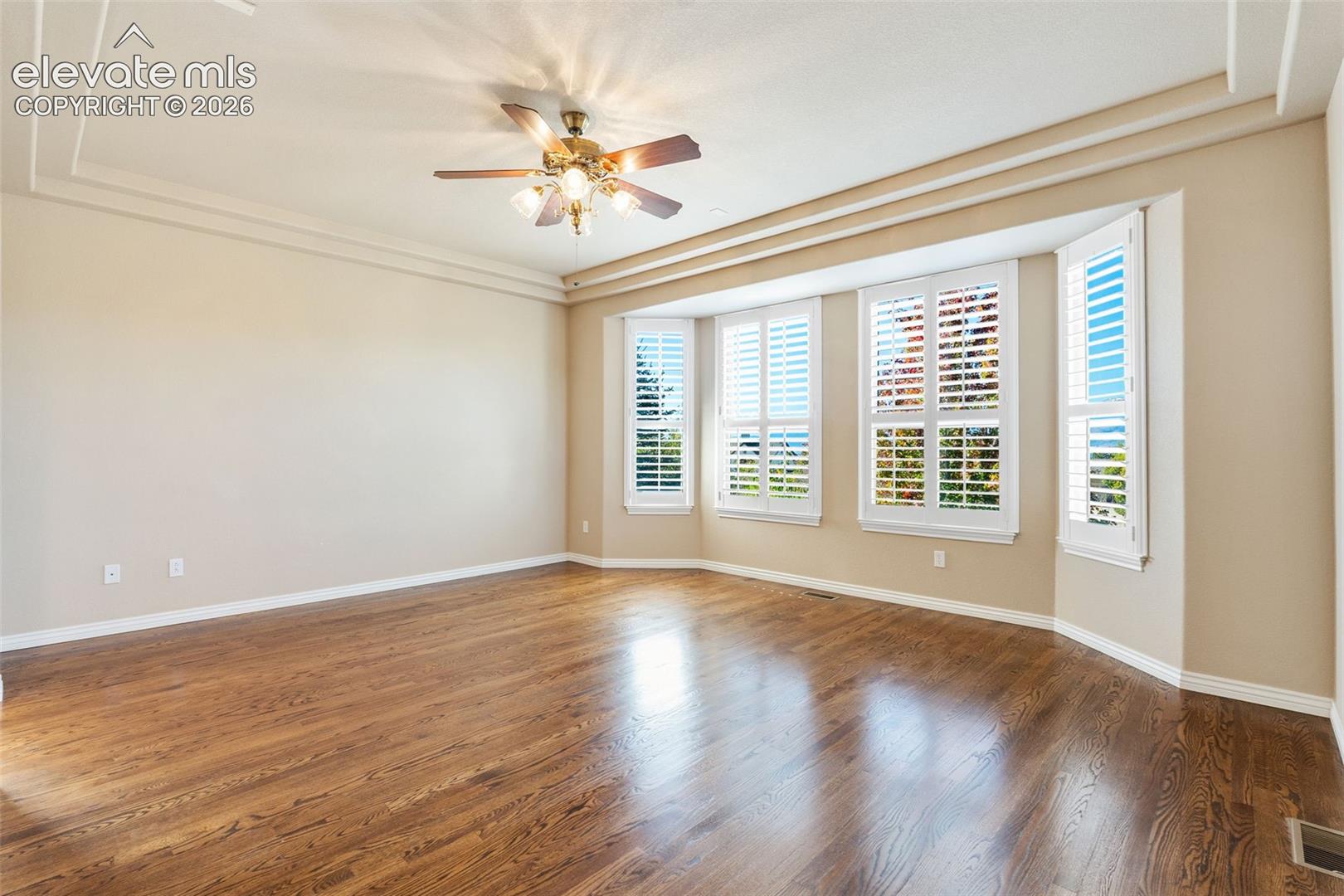 ADDITIONAL VIEW OF PRIMARY BEDROOM WITH HARDWOOD FLOORS, CEILING FAN AND WINDOWS WITH PLANTATION SHUTTERS