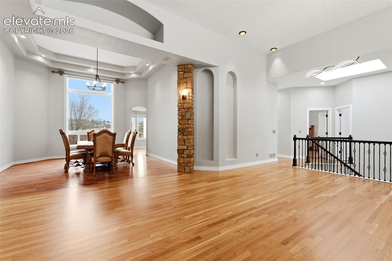 Spacious open-concept interior featuring light wood-finish flooring, a stone-clad pillar, and a modern chandelier