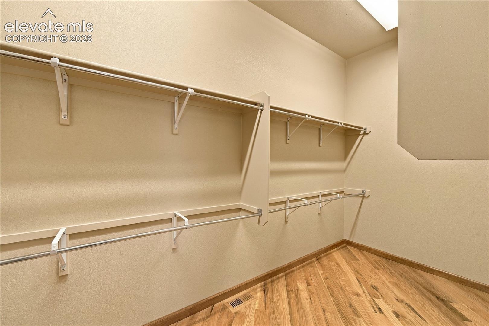 Walk-in closet featuring multi-level shelving, metal hanging rods, and wood-finish flooring