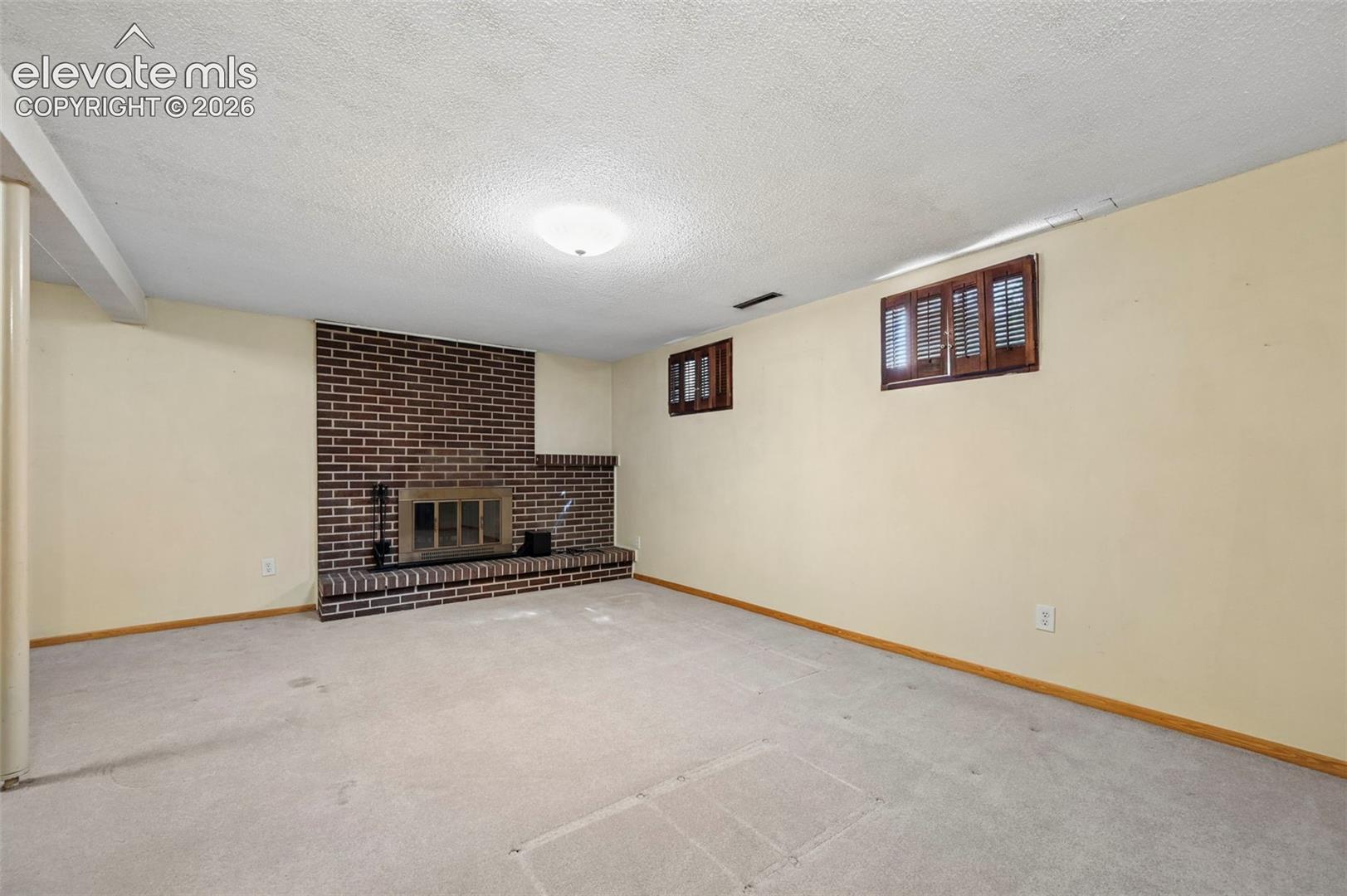 Lower Level featuring a brick fireplace with an integrated hearth, carpeted flooring, and wall-mounted windows with wood-finish shutters