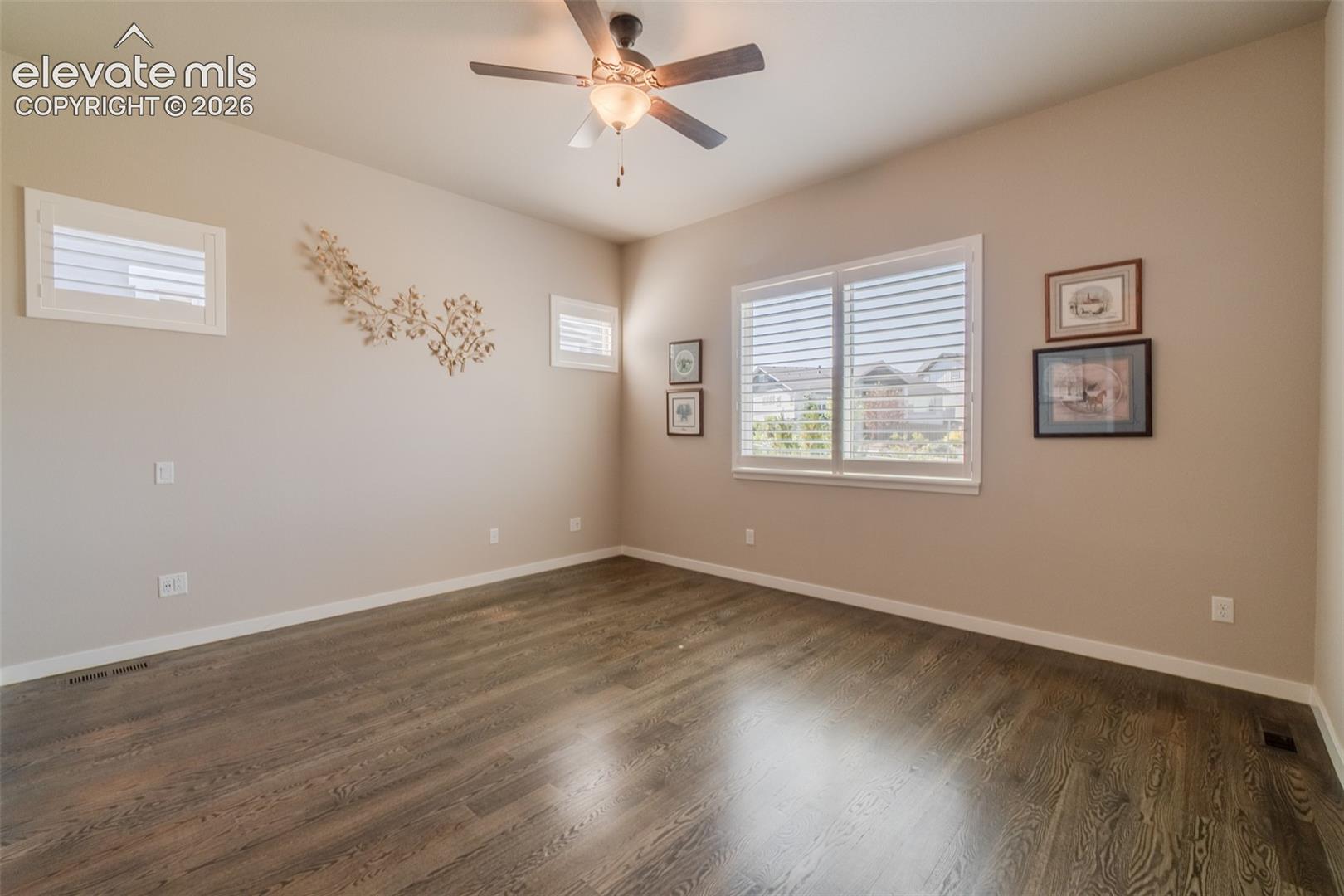 Spacious room featuring wood-finish flooring, neutral-toned walls, and a ceiling fan with integrated lighting