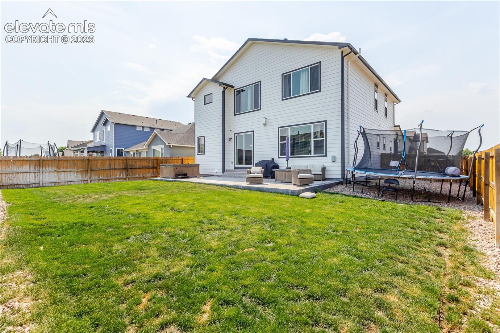 Two-story white siding exterior featuring a ground-level patio, expansive lawn, and a privacy fence