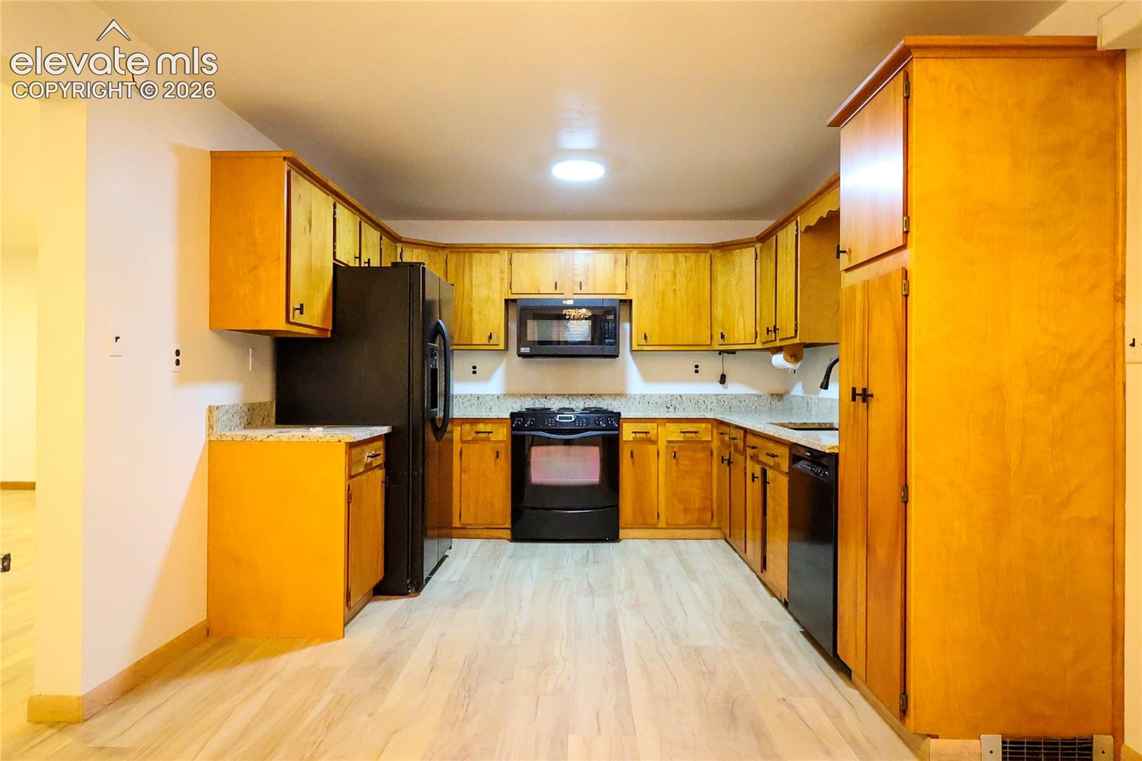 U-shaped kitchen with wood-finish cabinetry, light-toned countertops, and light wood-finish flooring