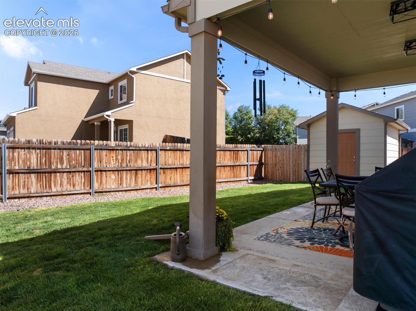 Expansive backyard featuring a covered concrete patio, wood privacy fence, and a detached storage shed