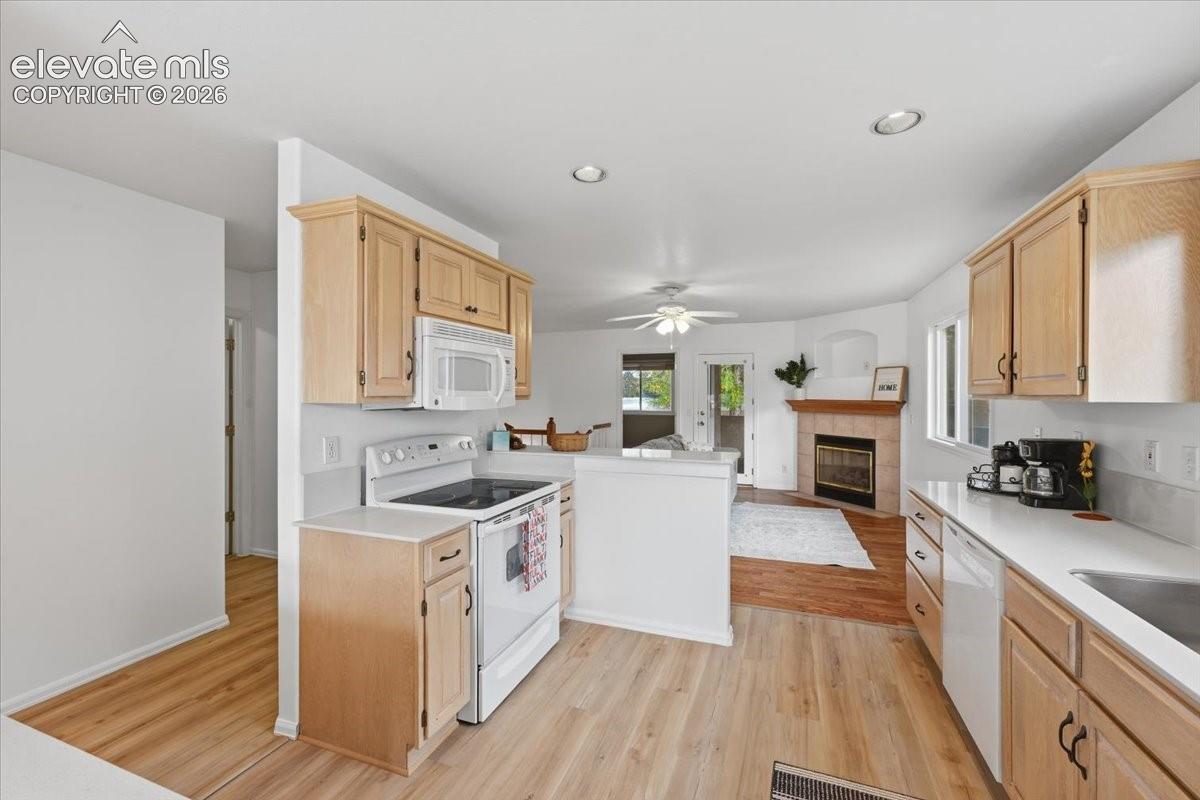 Kitchen featuring light-finish cabinetry, white countertops, a smooth-top range, and recessed lighting, paired with a fireplace featuring tile surround
