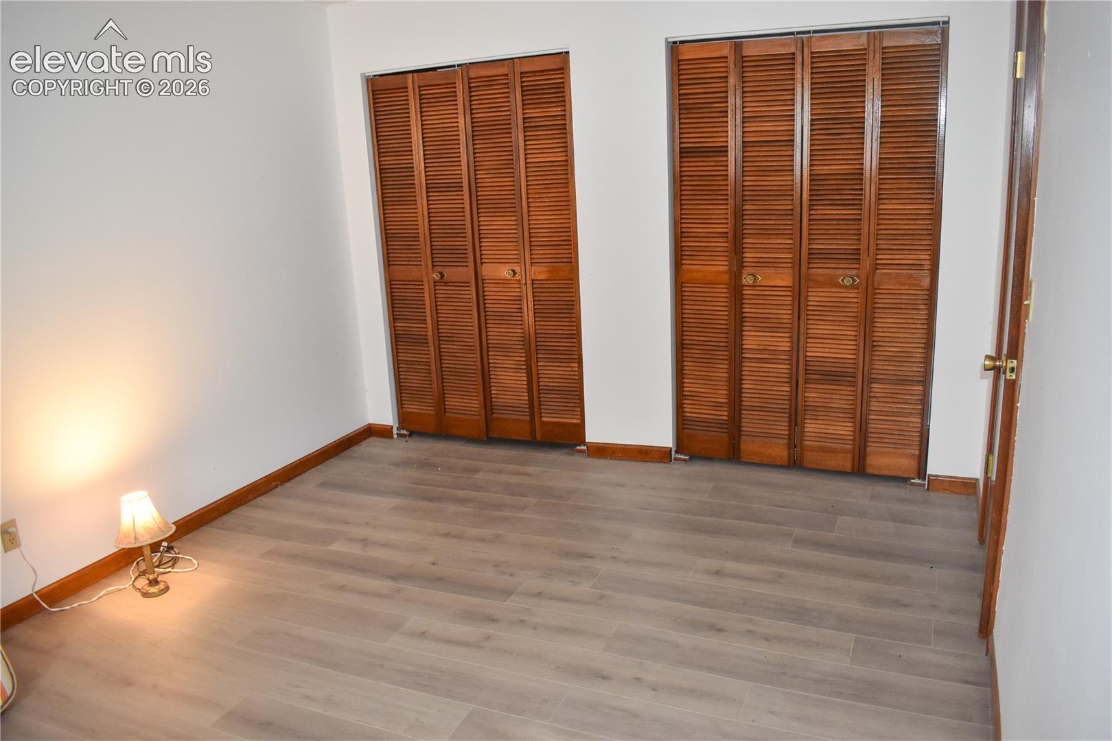 Two sets of bi-fold louvered closet doors, wood-finish flooring, and white painted walls