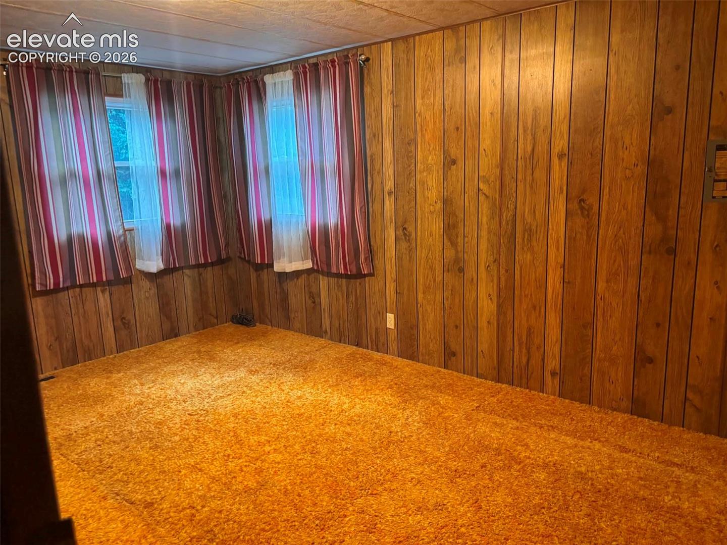 Interior room featuring wood-paneled walls, carpeted flooring, and two dual-pane windows