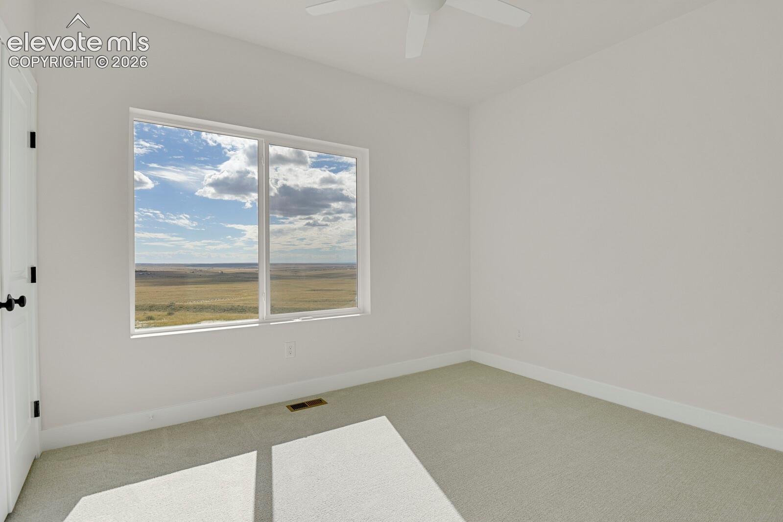 Neutral-toned wall finish, wall-to-wall carpeting, white-framed window with exterior landscape, and ceiling-mounted fan