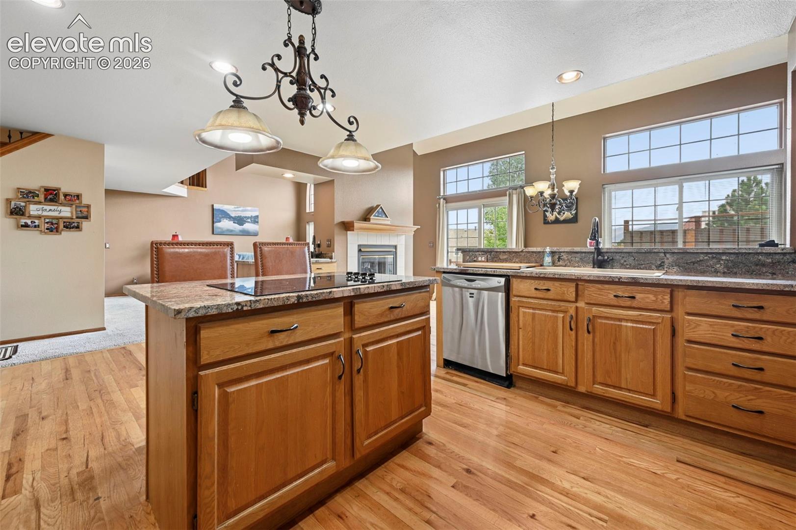 Wood-finish flooring, central island with cooktop, wood cabinetry, stainless steel dishwasher, and a fireplace with mantel