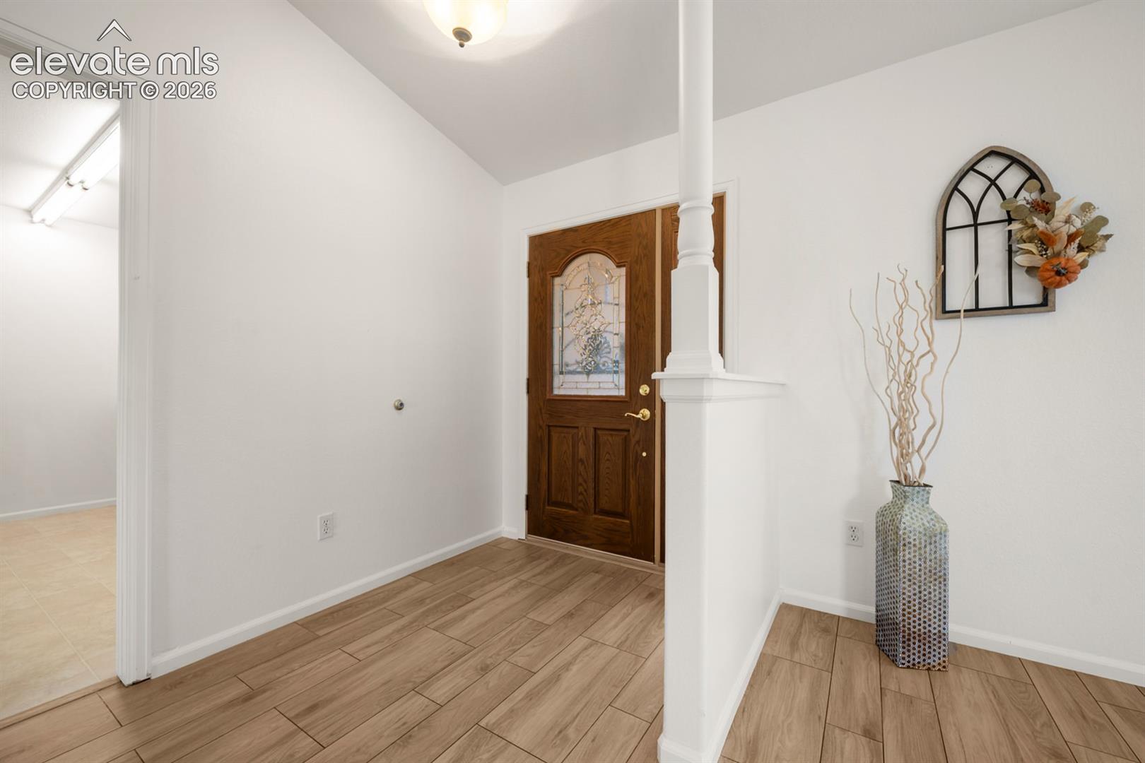 Entryway featuring wood-finish flooring, a vaulted ceiling, a wood-panel entry door with decorative glass inlay, and a partial partition wall with a column