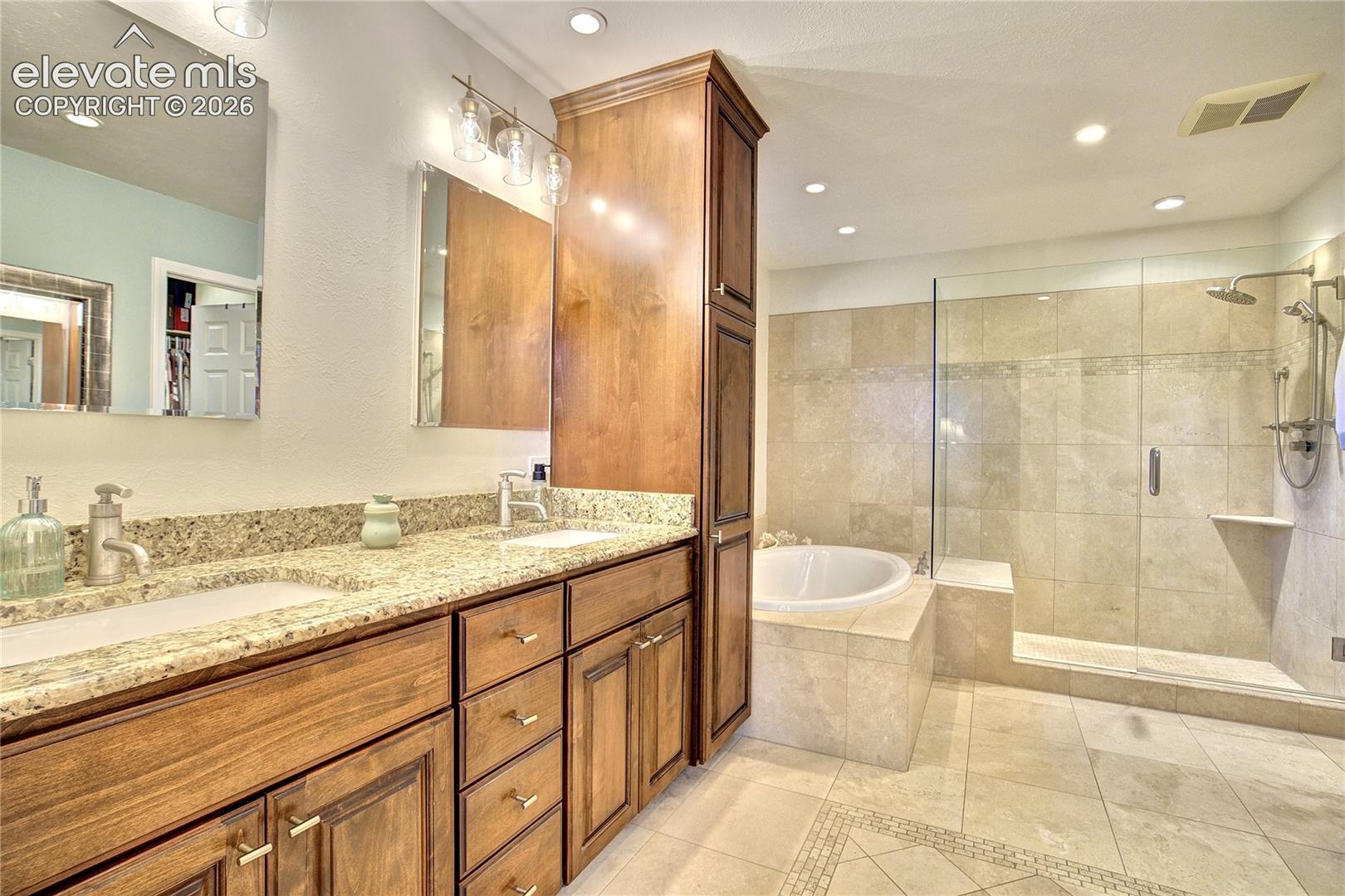 The updated 5-piece bath features travertine tile + a dual-sink granite vanity with integrated linen storage.