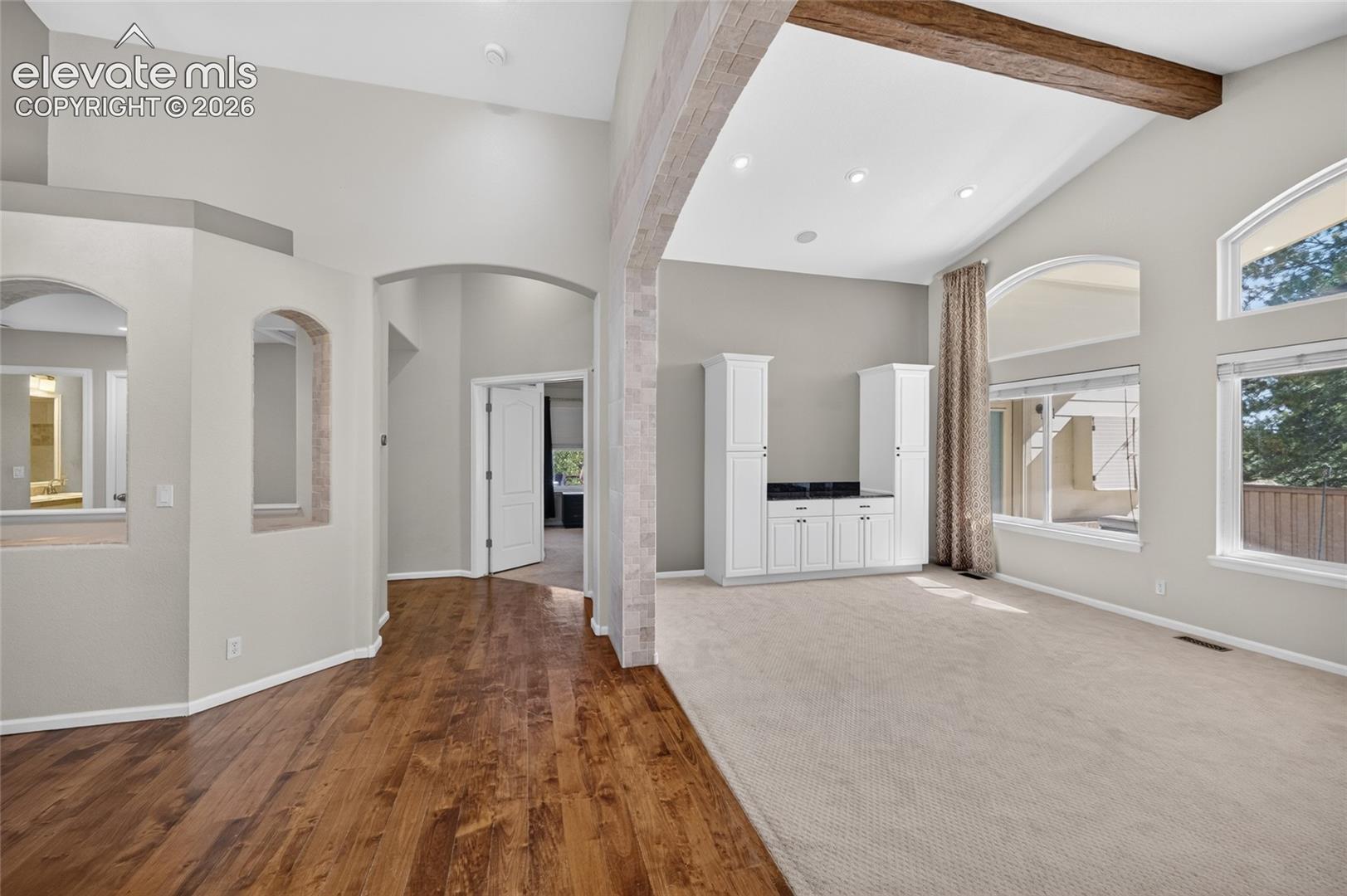 Vaulted ceilings with exposed wood beams, arched wall cutouts, built-in cabinetry with a dark stone countertop, and multi-pane windows with arched transoms