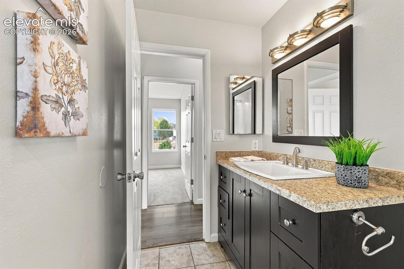 Dark-toned cabinetry featuring a stone-composite countertop, integrated white sink, framed vanity mirror, and multi-bulb wall lighting