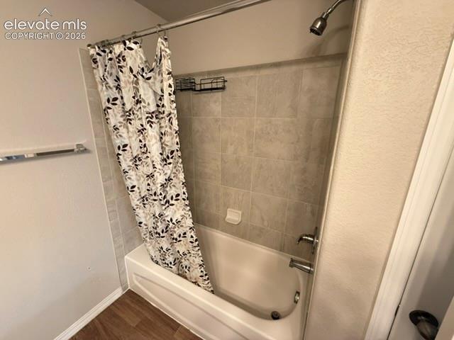 Bathtub with tiled surround, brushed nickel fixtures, and wood-finish flooring