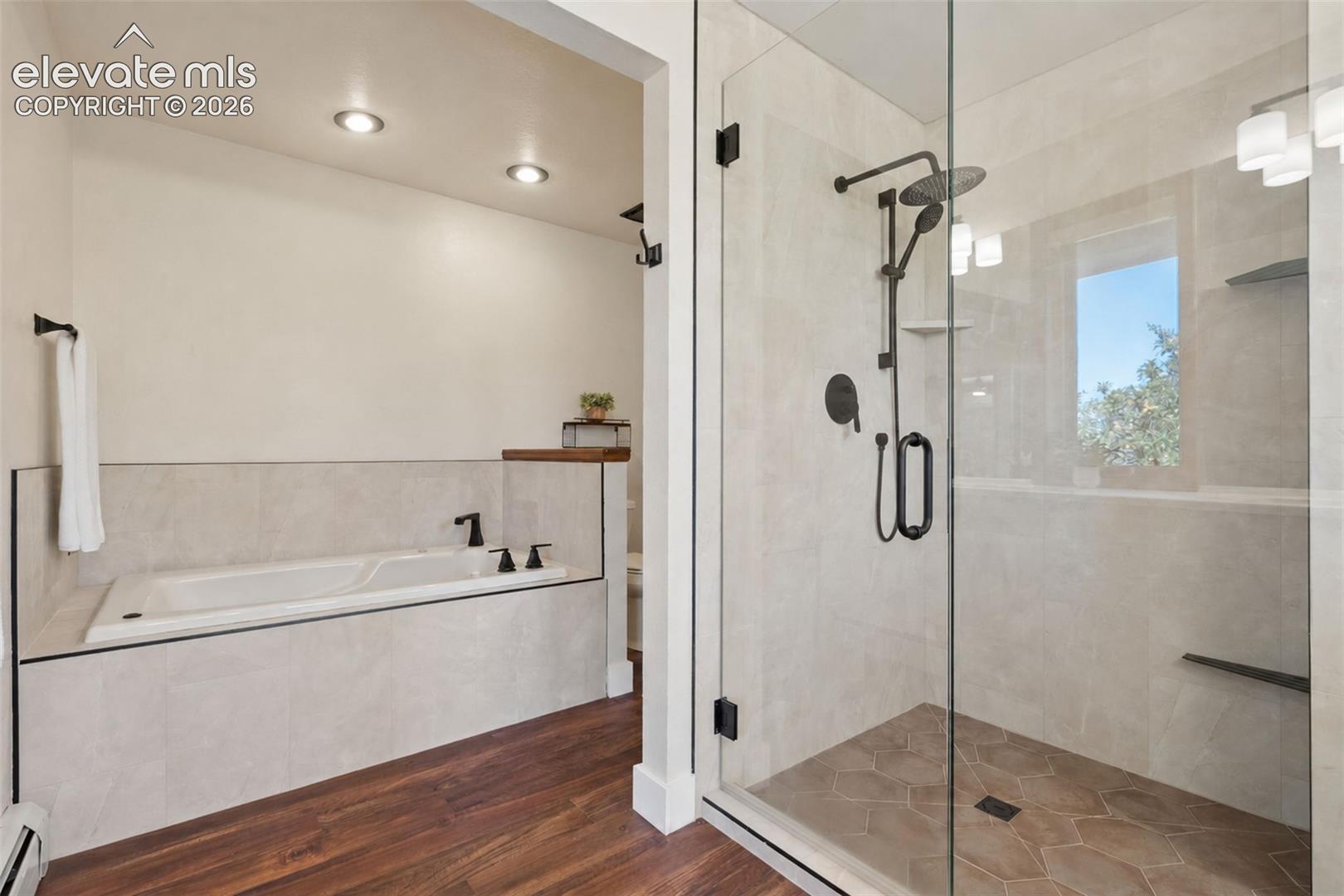Glass-enclosed shower with matte black fixtures, an integrated tub, and wood-finish flooring