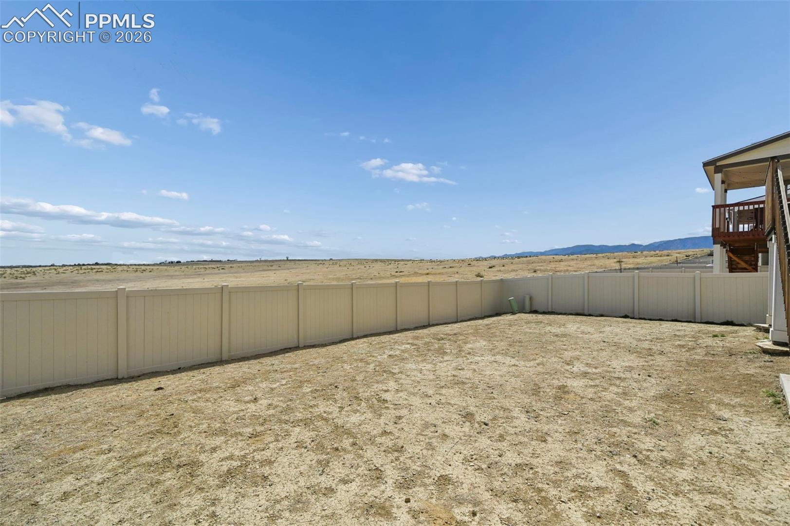 Expansive rear yard with a perimeter fence, a partially covered deck, and distant mountain scenery