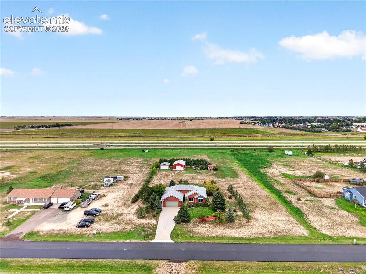 Aerial perspective featuring a single-story residence with a red brick exterior, a paved driveway, multiple mature trees, and a detached outbuilding on expansive acreage
