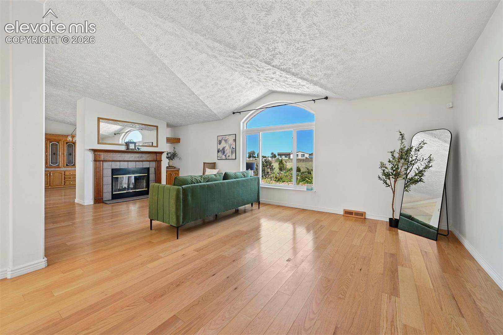 Hardwood flooring throughout, vaulted ceiling, arched window, fireplace with tile surround and wood mantel, built-in cabinetry