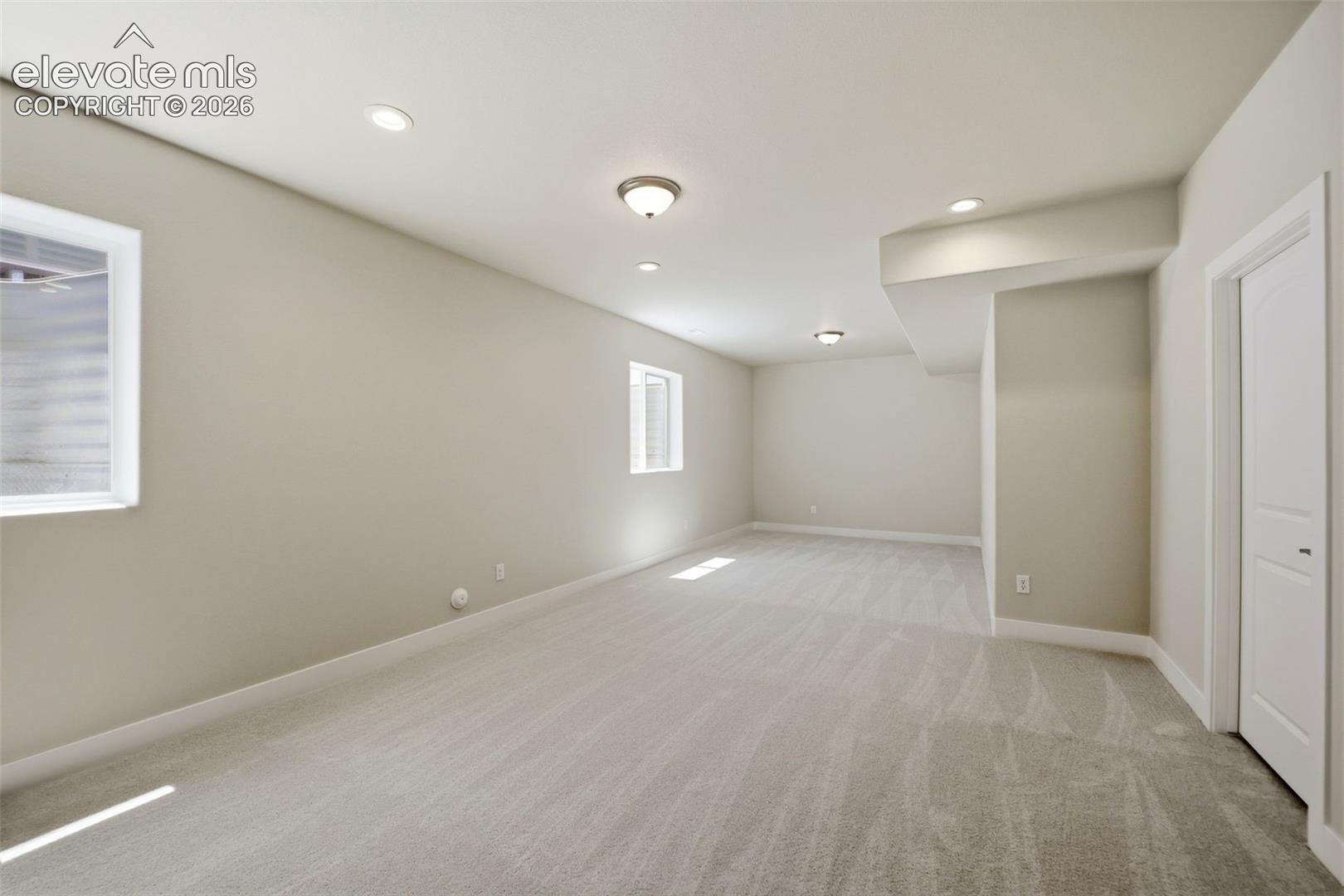 Neutral-toned interior space featuring neutral wall-to-wall carpeting, recessed and surface-mounted lighting, and two windows