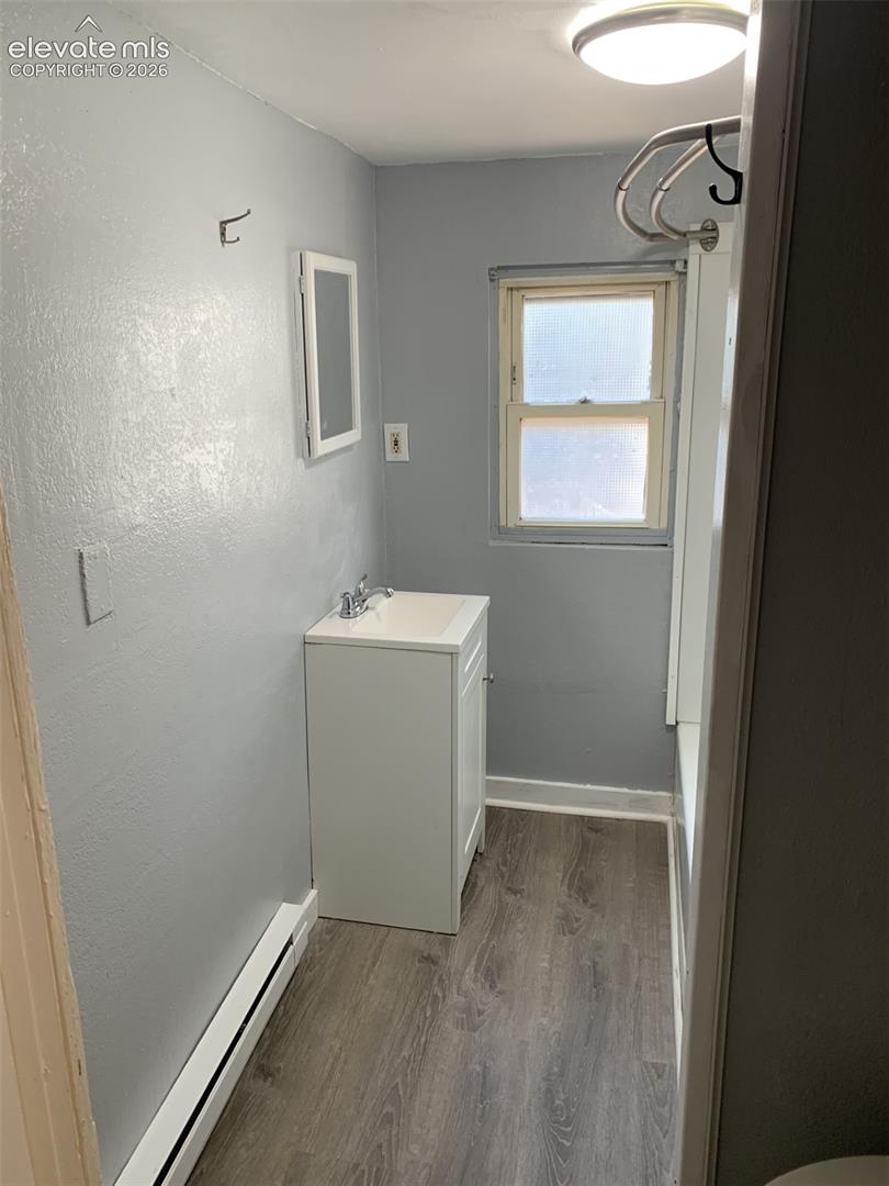 Wood-finish flooring, single vanity with integrated sink, wall-mounted medicine cabinet, and a window with privacy glass