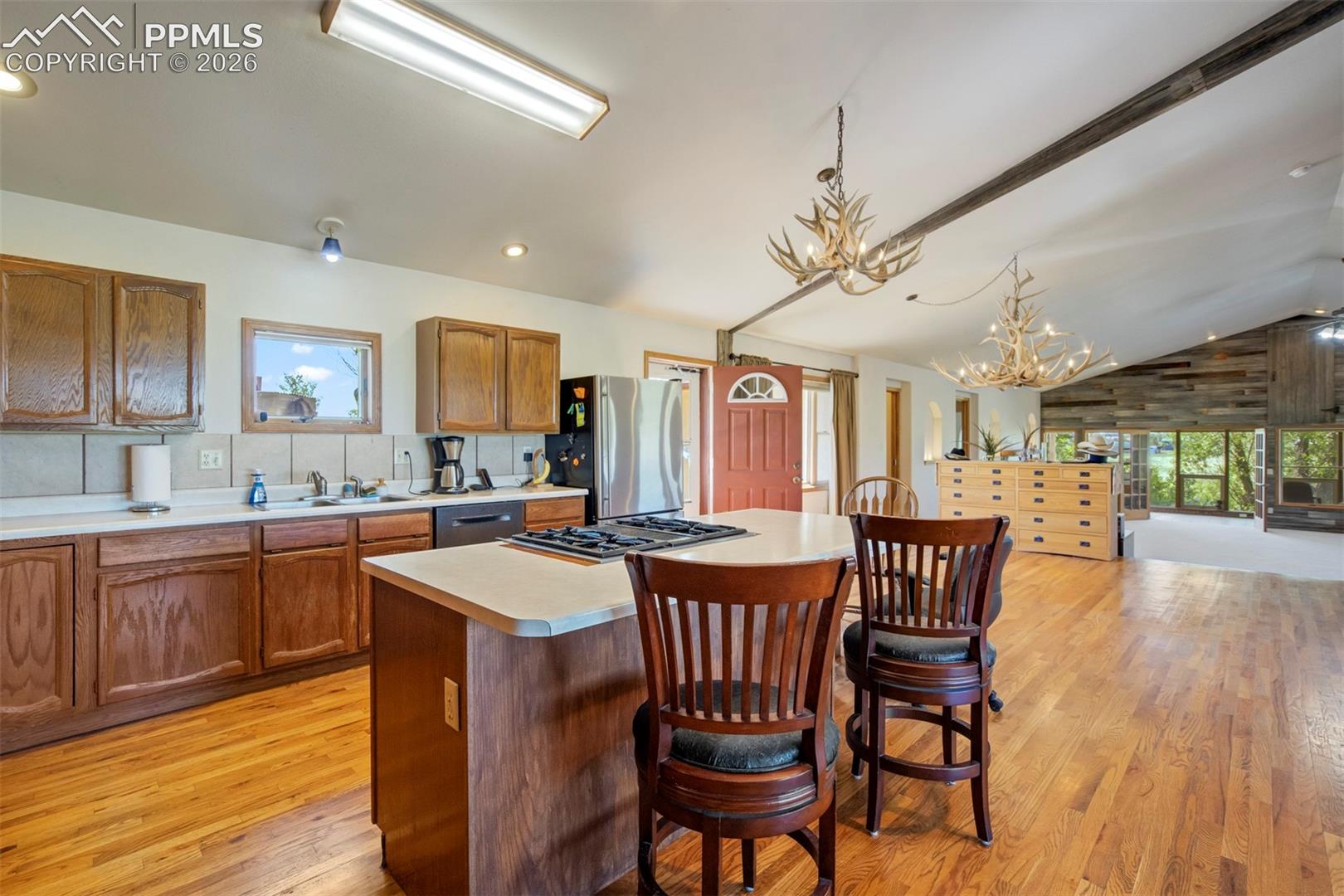 Open-concept kitchen featuring wood cabinetry, a central island with integrated cooktop, and light-toned countertops