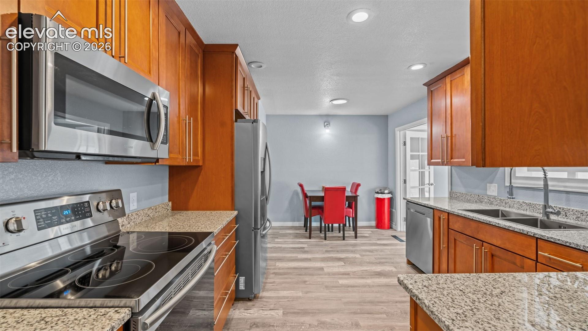 Kitchen featuring wood cabinetry, stainless steel appliances, speckled countertops, and wood-finish flooring