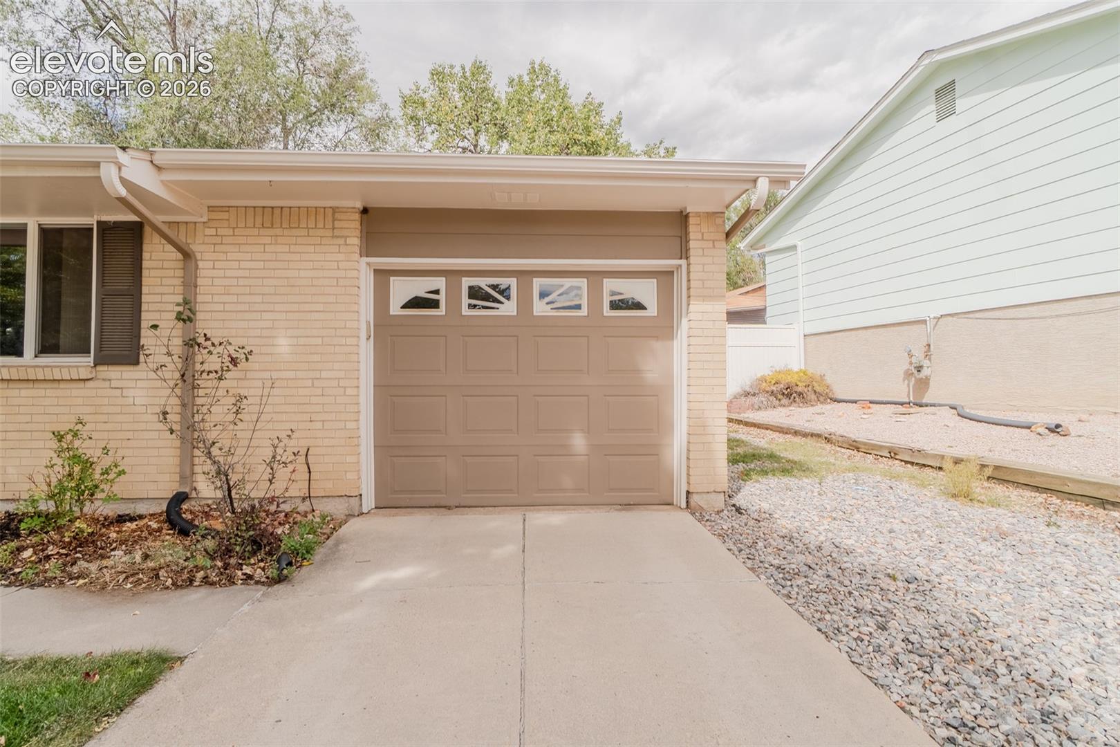 Brick exterior with a single-car garage featuring decorative window inserts, concrete driveway, and side yard with gravel landscaping