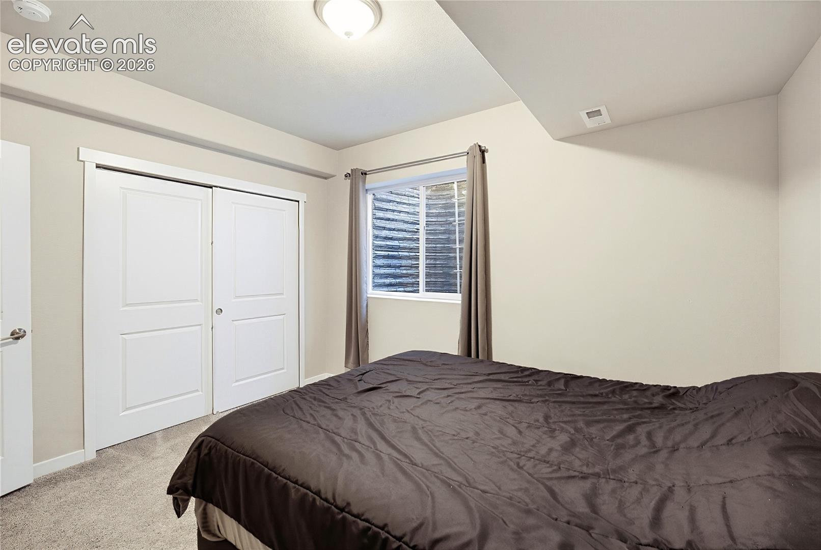 Room featuring neutral wall paint, carpeted flooring, a recessed window with a corrugated steel window well, and a closet with dual paneled doors