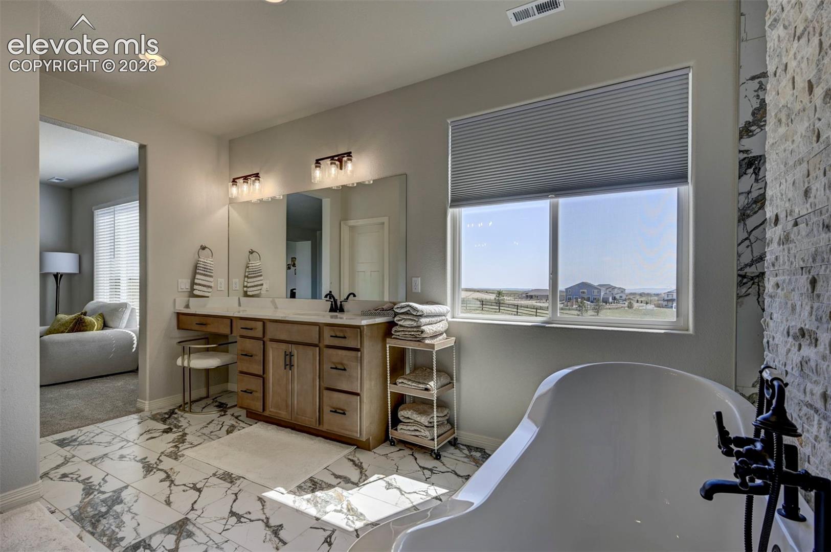 Bathroom featuring a freestanding tub with matte black fixtures, a dual-sink vanity with light wood cabinetry, and patterned floor tile