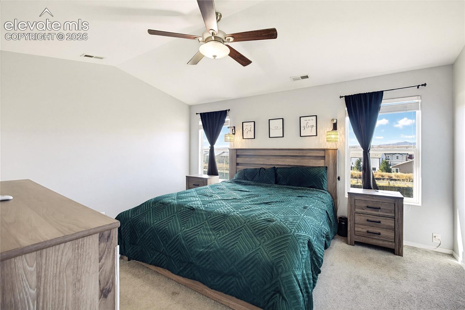 Vaulted ceiling with a ceiling fan, dual windows, and carpeted flooring