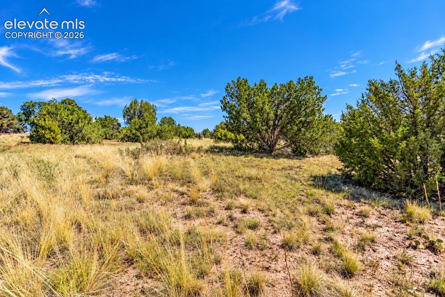 Sweeping aerial perspective of rolling juniper-covered hills, winding rural roads, and expansive high-desert terrain stretching toward the horizon.

