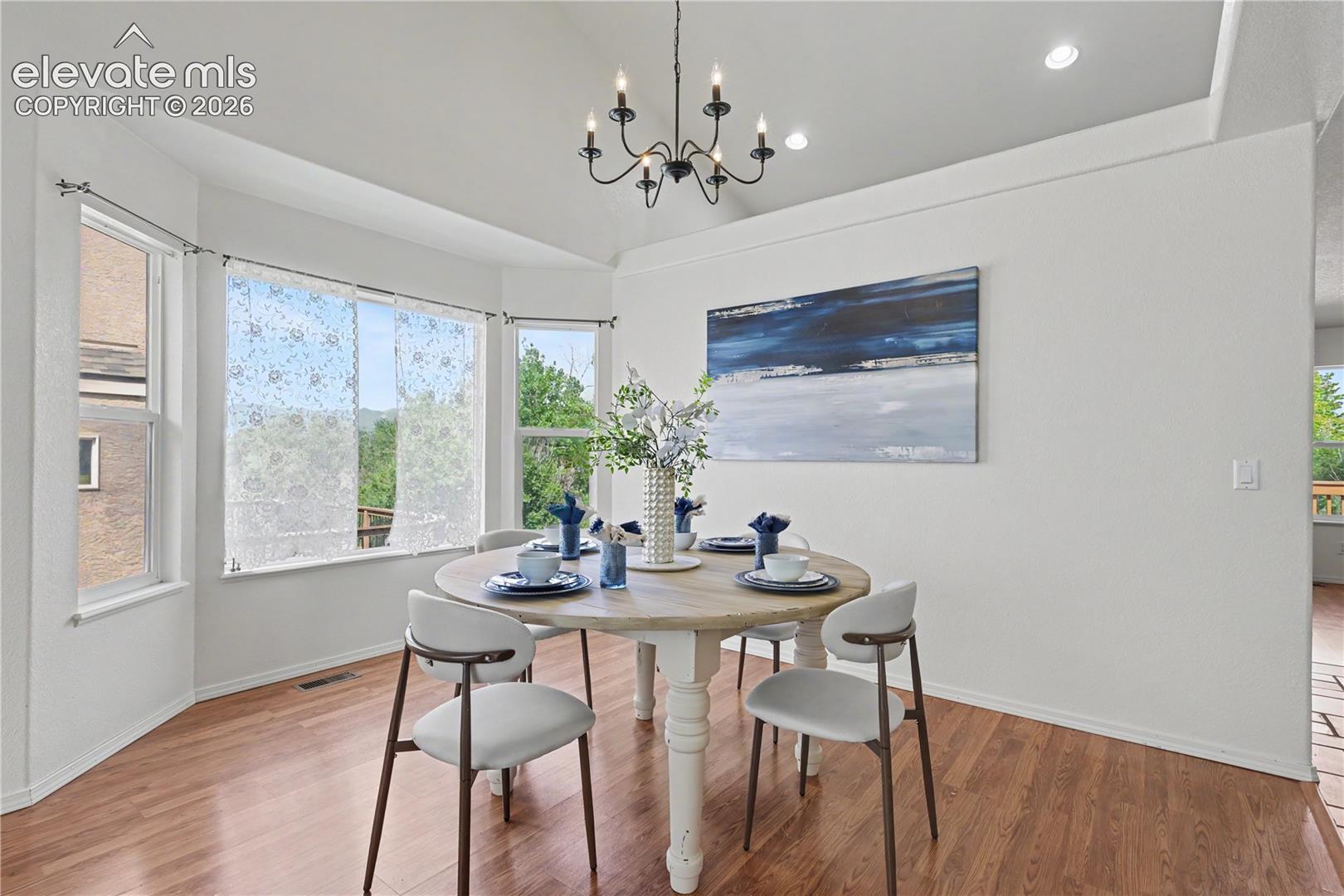 Bay window dining area featuring wood-finish flooring, a contemporary chandelier, recessed lighting, and white walls