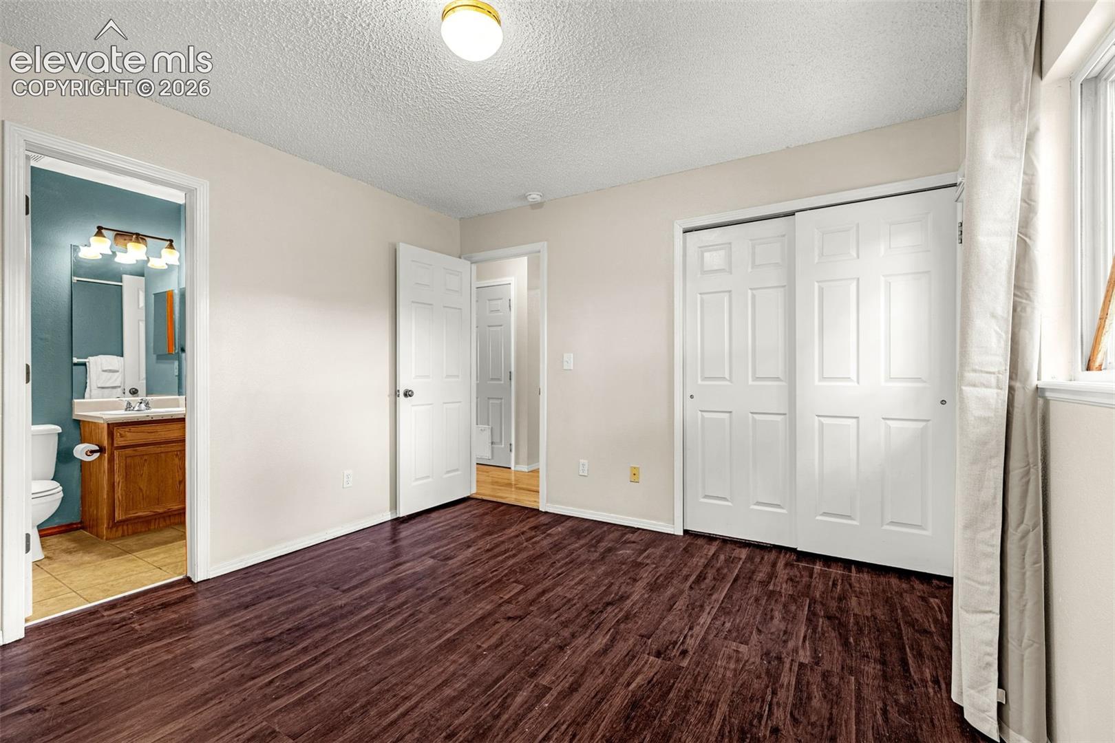 Bedoom featuring dark wood-finish flooring, light-toned walls, and a window with curtain rod