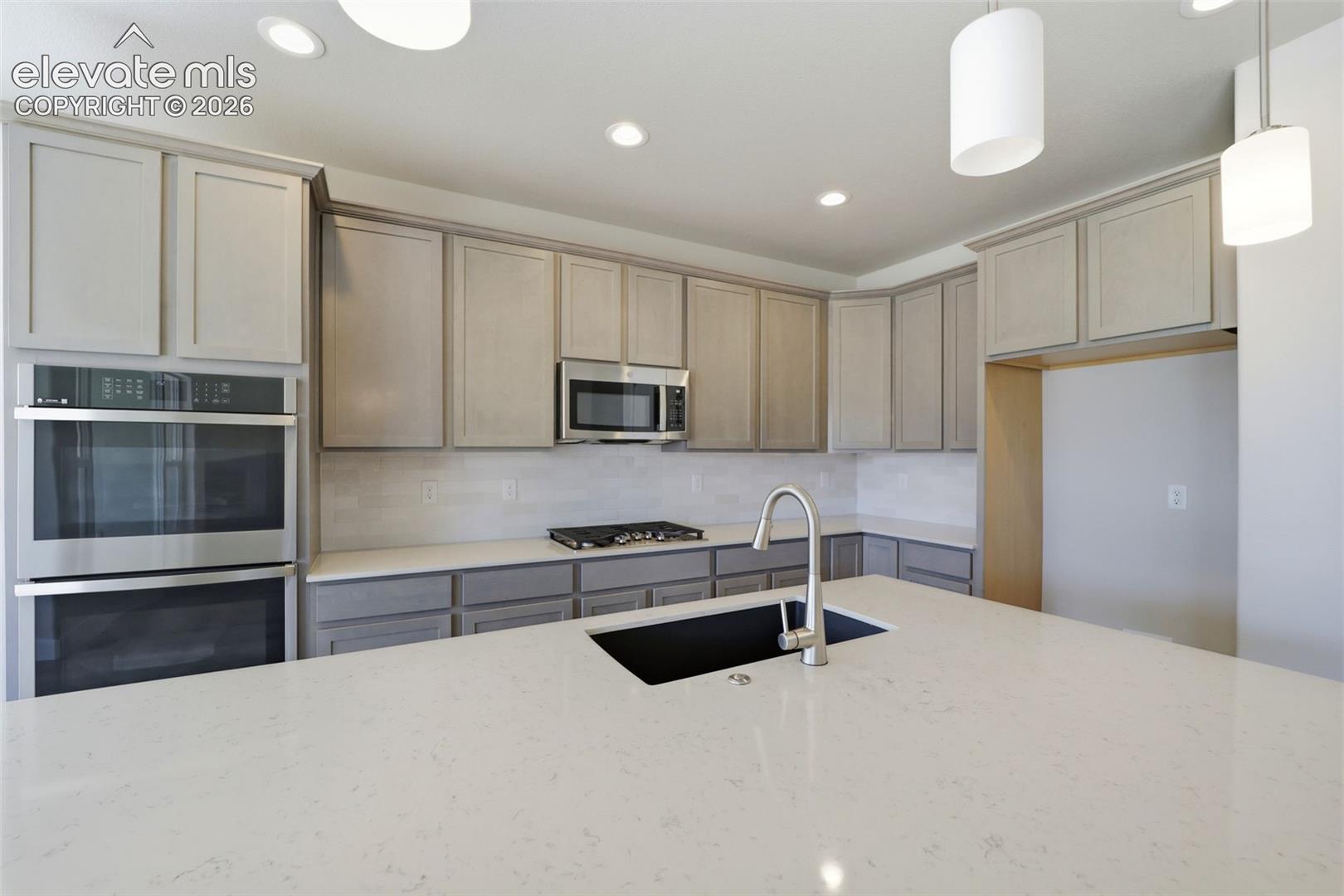 Kitchen featuring light-toned cabinetry, quartz countertops, an expansive center island with an undermount sink, stainless steel double wall ovens, and a built-in microwave