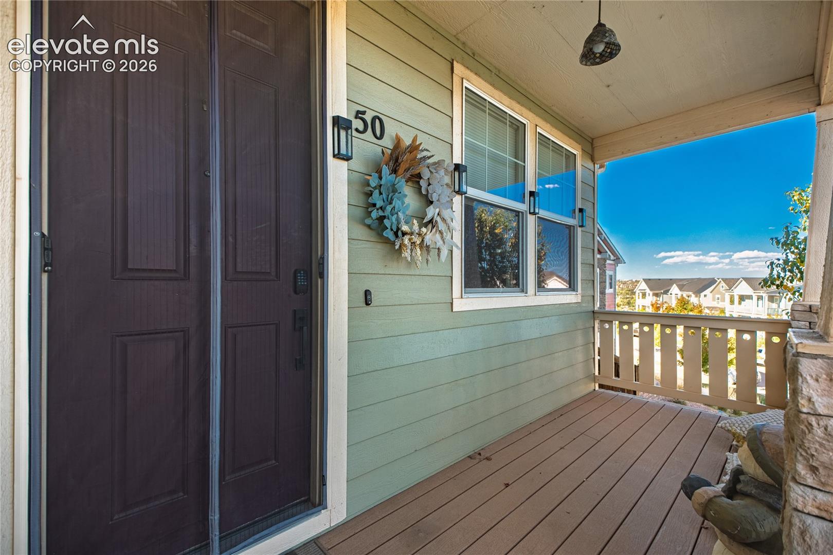 Covered front porch featuring wood-finish decking, horizontal lap siding, stone masonry accents, and wall-mounted exterior lighting