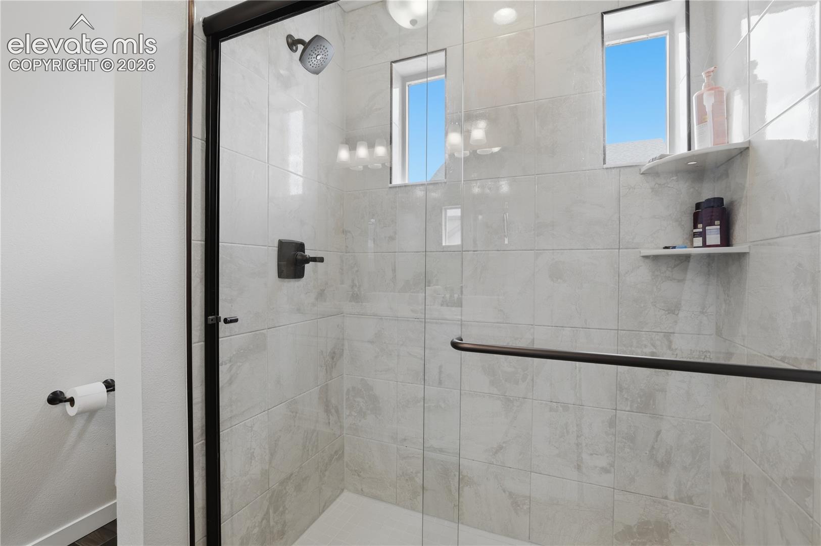 Shower enclosure with a black-framed glass door, tiled walls, a dark bronze shower fixture, and built-in shelving