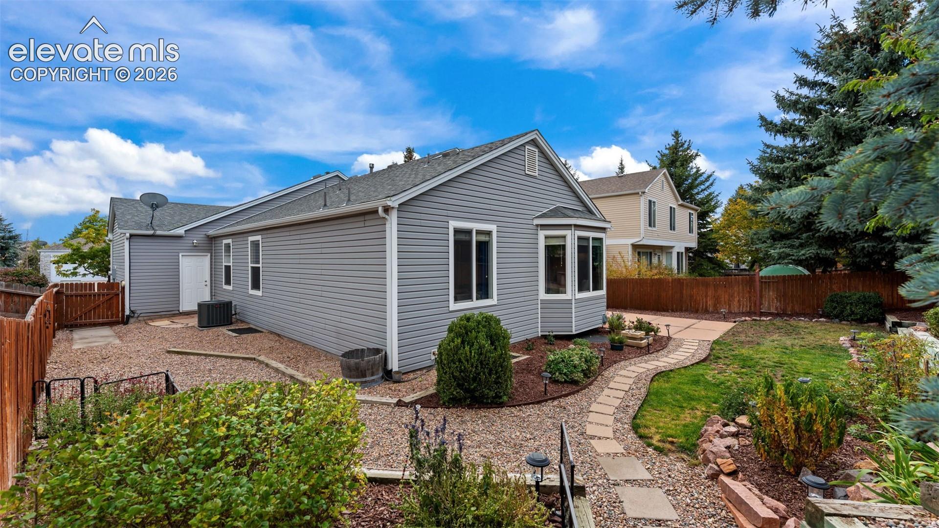Exterior featuring horizontal siding, bay window, stone paver pathway, gravel landscaping, and perimeter wood fencing