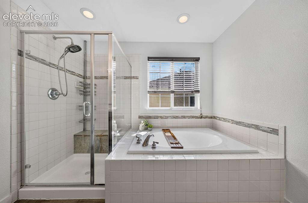 Glass-enclosed shower with a built-in bench, accompanied by a spacious soaking tub