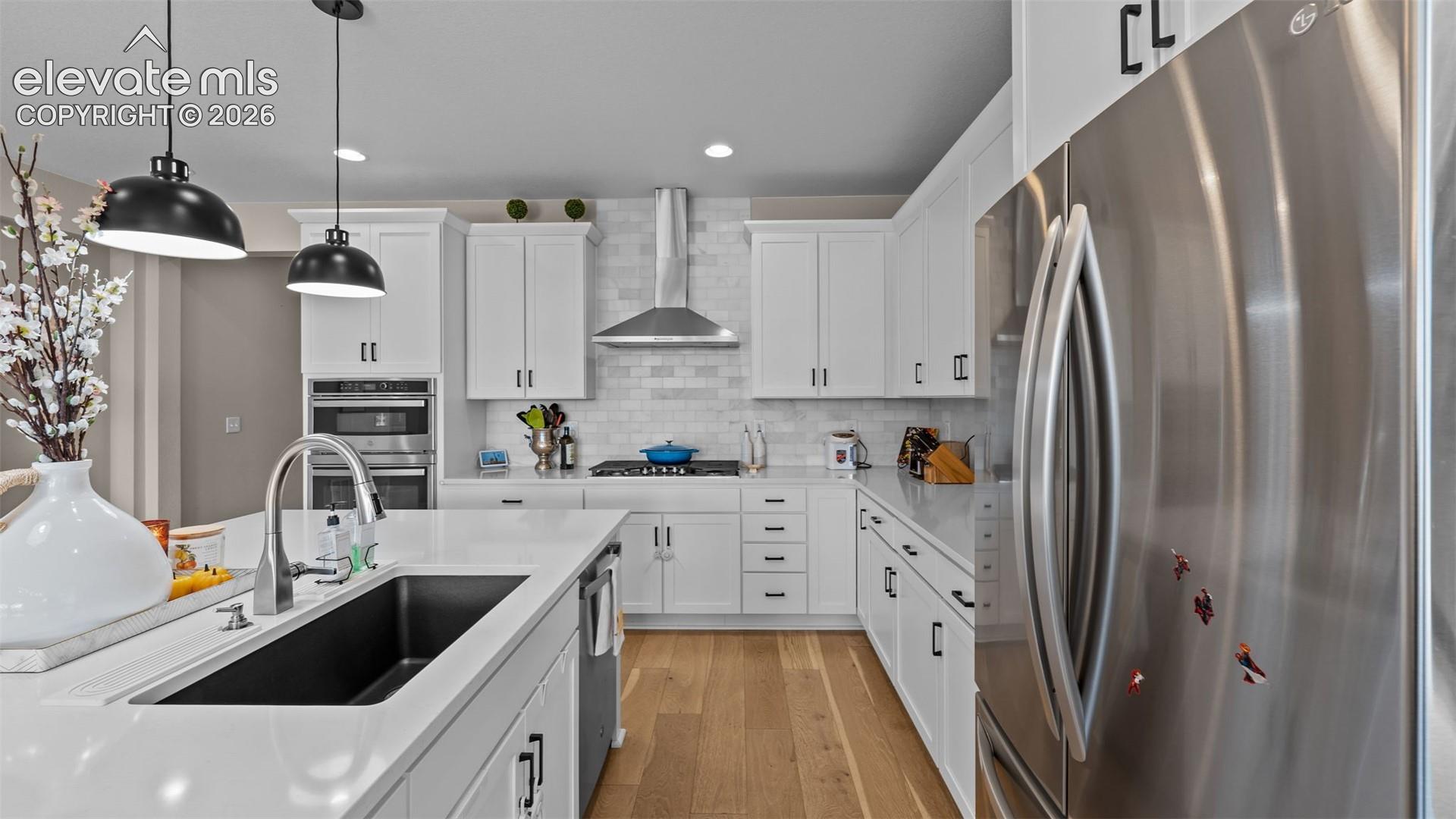 Kitchen featuring white cabinetry, stainless steel appliances, a white tile backsplash, a large island with an undermount sink, and wood-finish flooring