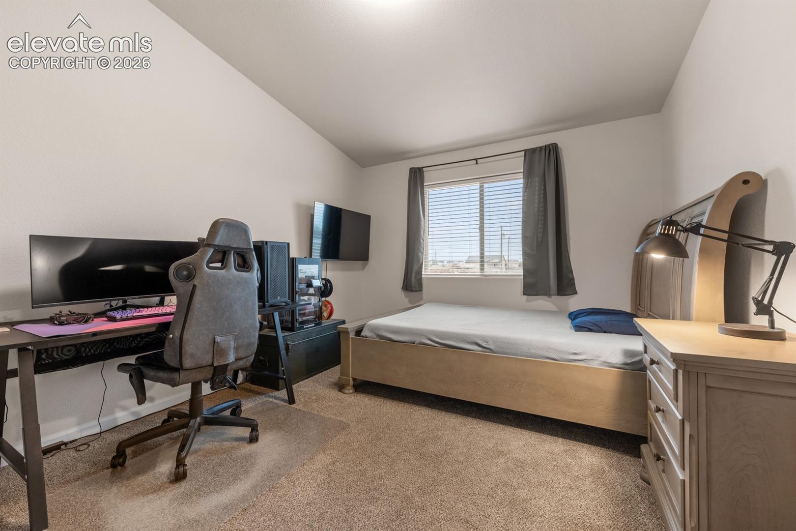 Neutral-toned room featuring high-set vaulted ceilings, carpeted flooring, and a window with horizontal blinds