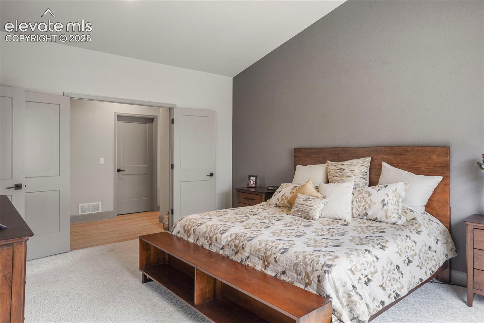 Bedroom featuring a light grey accent wall, white textured carpet flooring, and a natural wood headboard