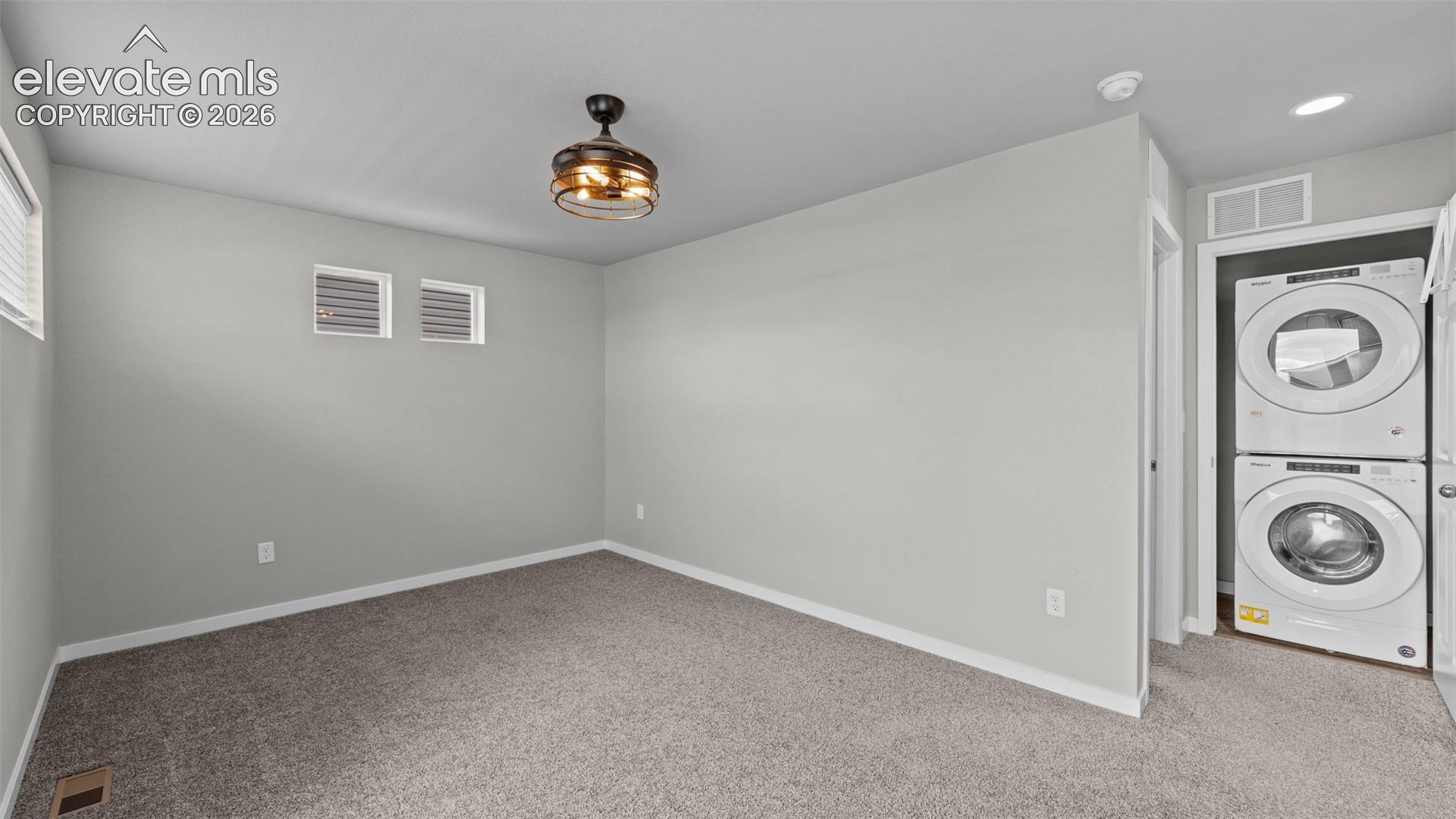 Neutral-toned carpeting, high-positioned rectangular windows, flush-mount lighting fixture, and a built-in stackable laundry unit