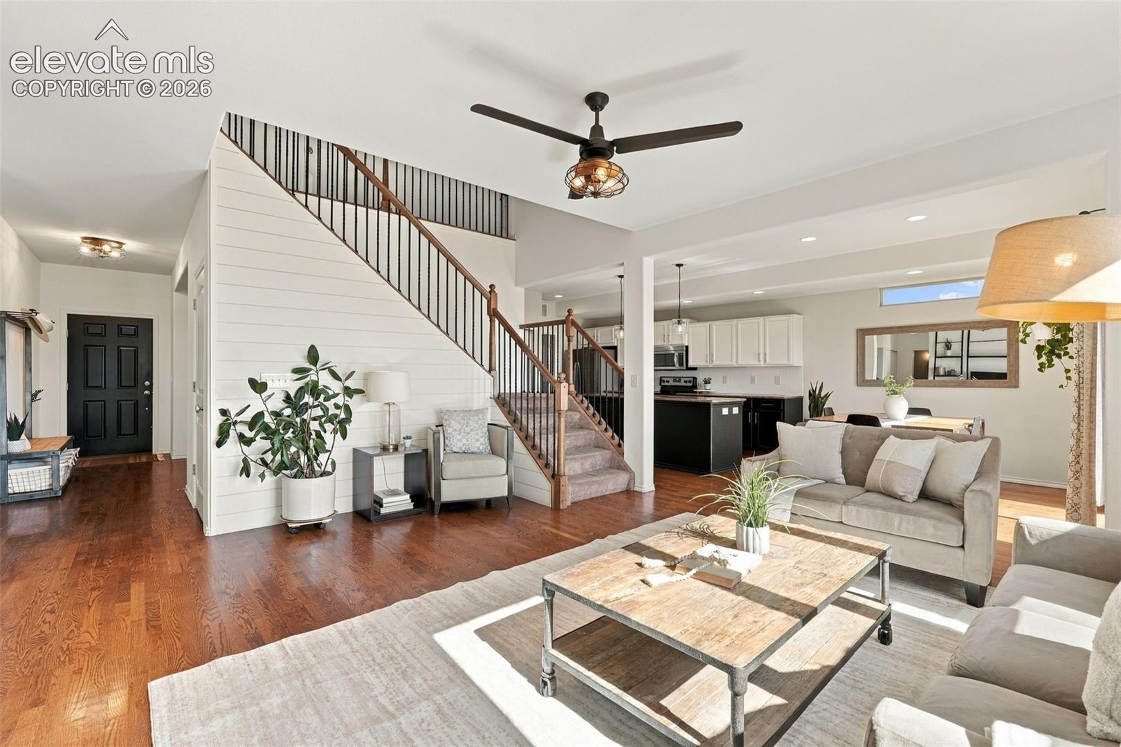 Open-concept interior featuring wood-finish flooring, horizontal shiplap wall accents, a staircase with metal balusters, a ceiling fan with integrated lighting, and recessed ceiling lights