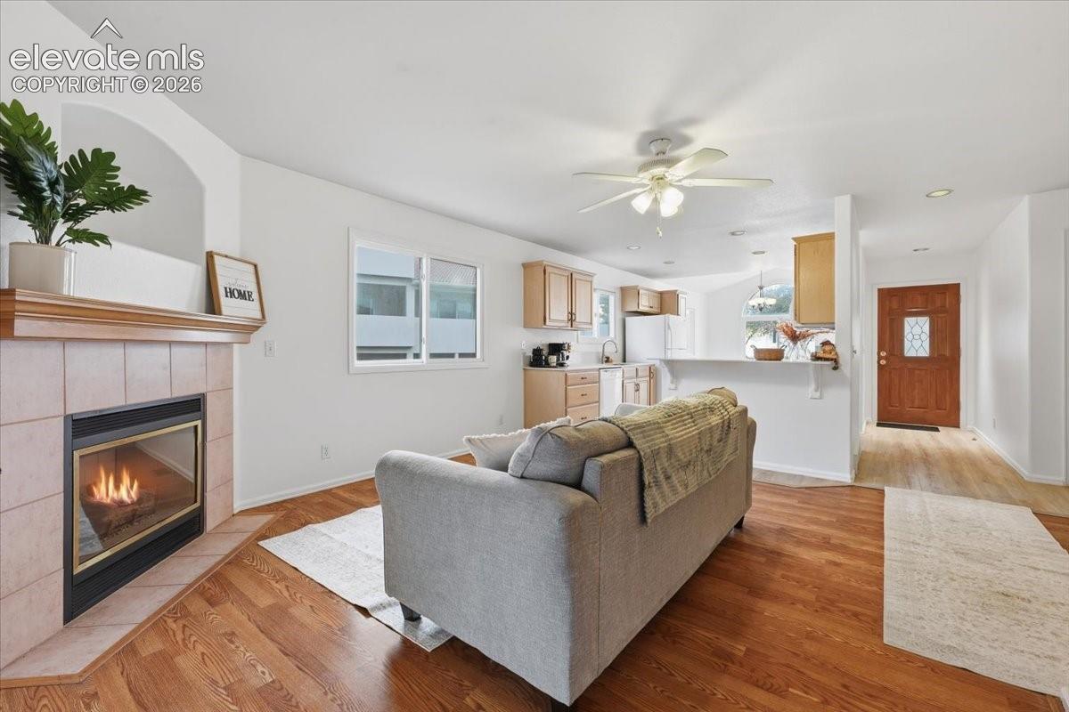 Living area featuring a fireplace with a tile surround and mantle, wood-finish flooring, ceiling fan, and recessed lighting