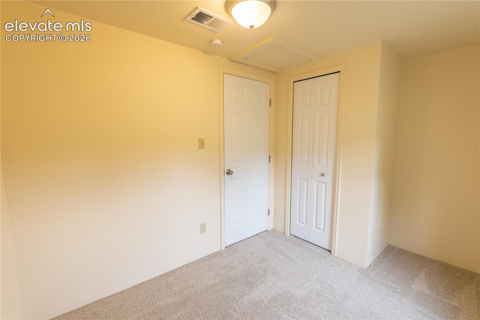 Neutral-toned interior room featuring wall-to-wall carpeting, two white paneled doors, and a flush-mount ceiling light fixture