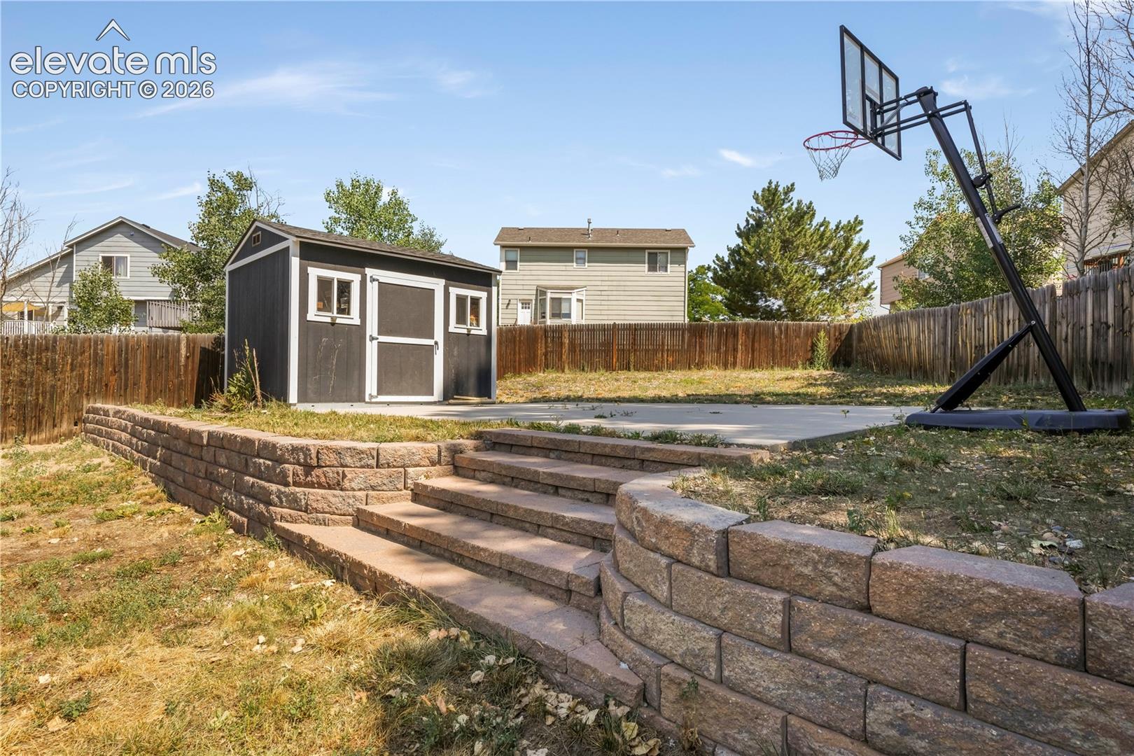 Back of home with large backyard patio, multiple levels, basketball goal and shed for storage