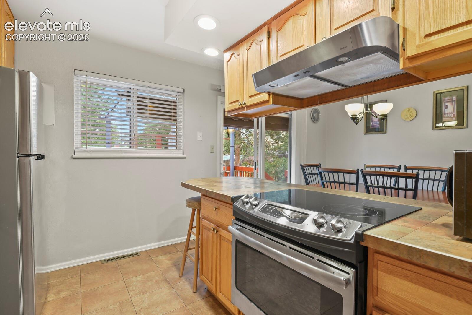 Kitchen featuring a stainless steel range with a flat cooktop, wood cabinetry, tile countertops, and recessed lighting