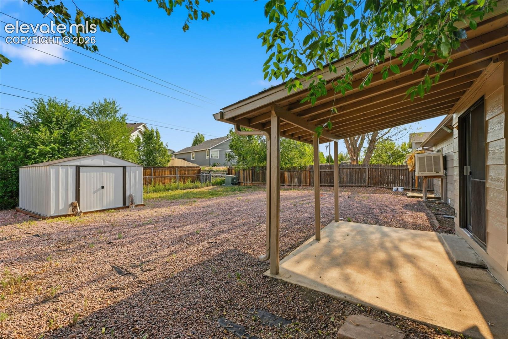 Expansive outdoor space featuring a covered patio, gravel landscaping, a storage shed, and a privacy fence