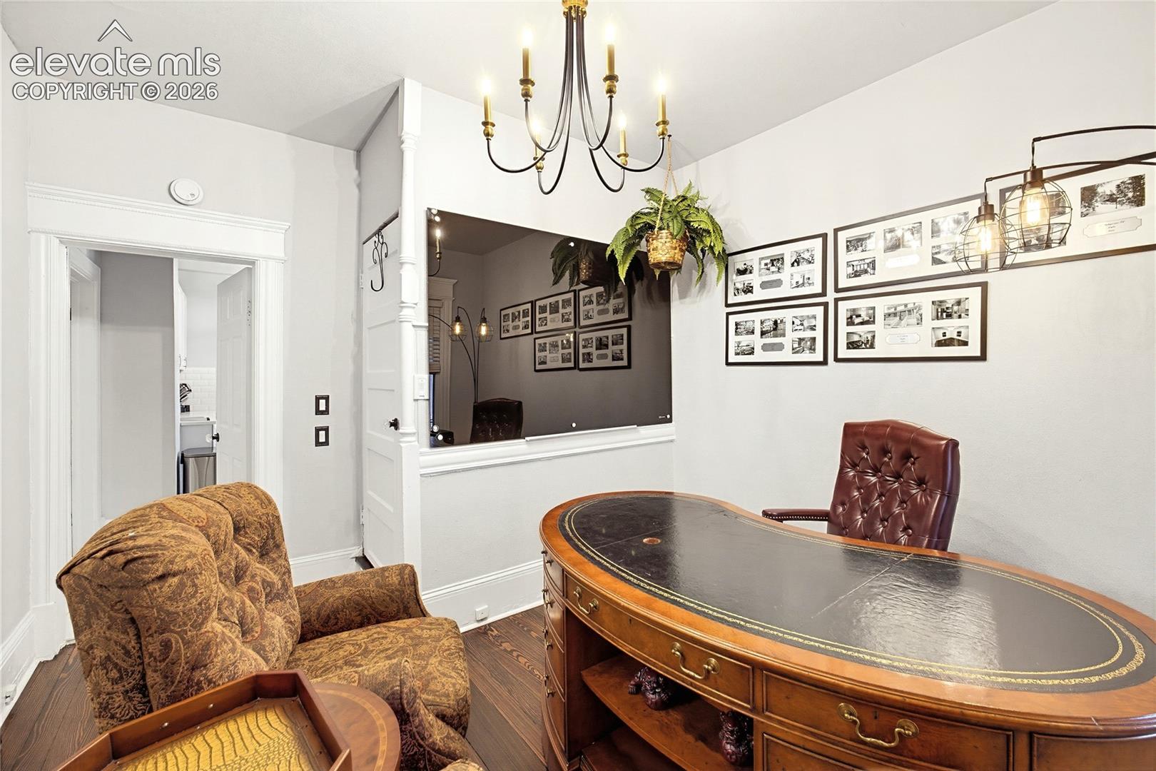 Hardwood flooring, cased doorway, overhead chandelier, wall-mounted light fixture, and white wall finishes
