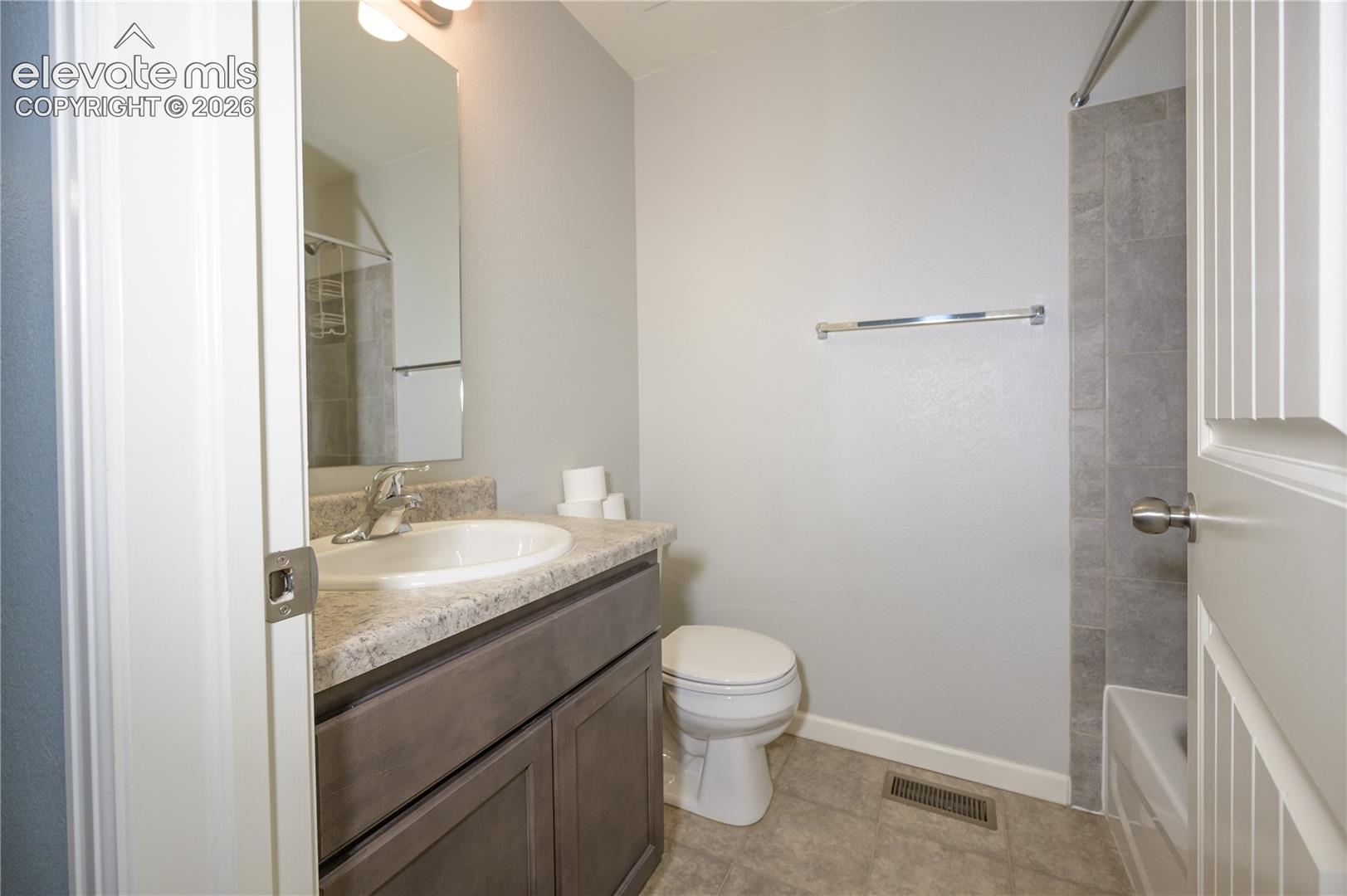 Bathroom featuring a vanity with shaker-style cabinetry, stone-finish countertop with an integrated oval sink, wall-mounted mirror, and tile-surround shower enclosure